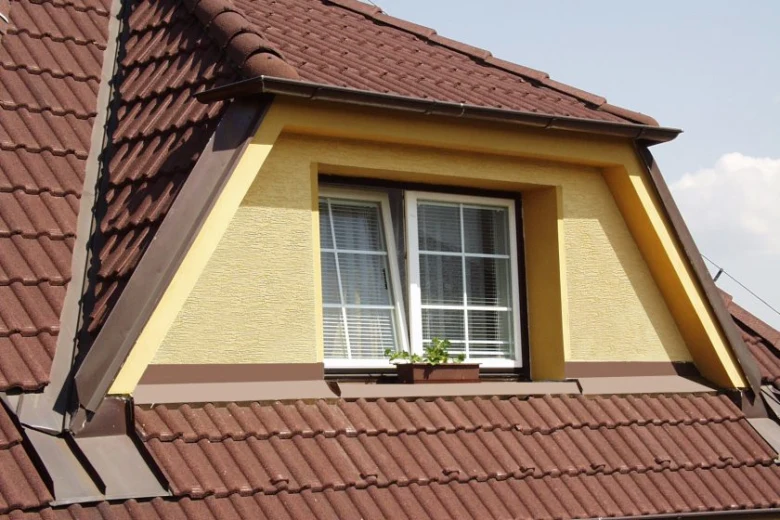 Moderní vikýř s bílými okny v žluté fasádě na hnědé střech.