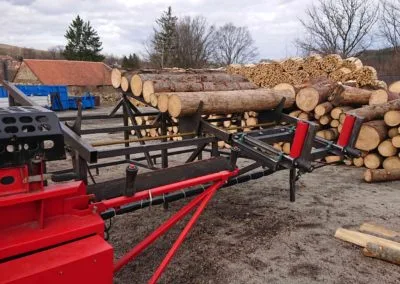 Červený stroj na zpracování dříví s naloženými kmeny.