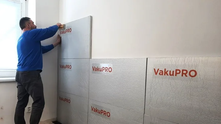 Muž montuje vakuové izolační panely na stěnu.