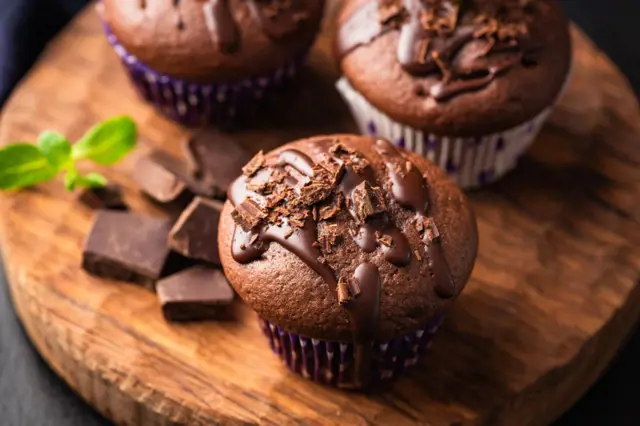 Čokoládové muffiny s čokoládovou polevou na dřevěném talíři.