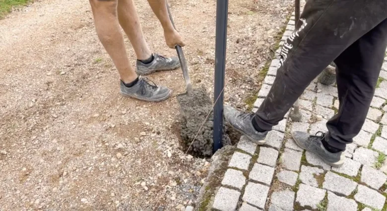 Dva lidé zalévají beton kolem plotového sloupku.
