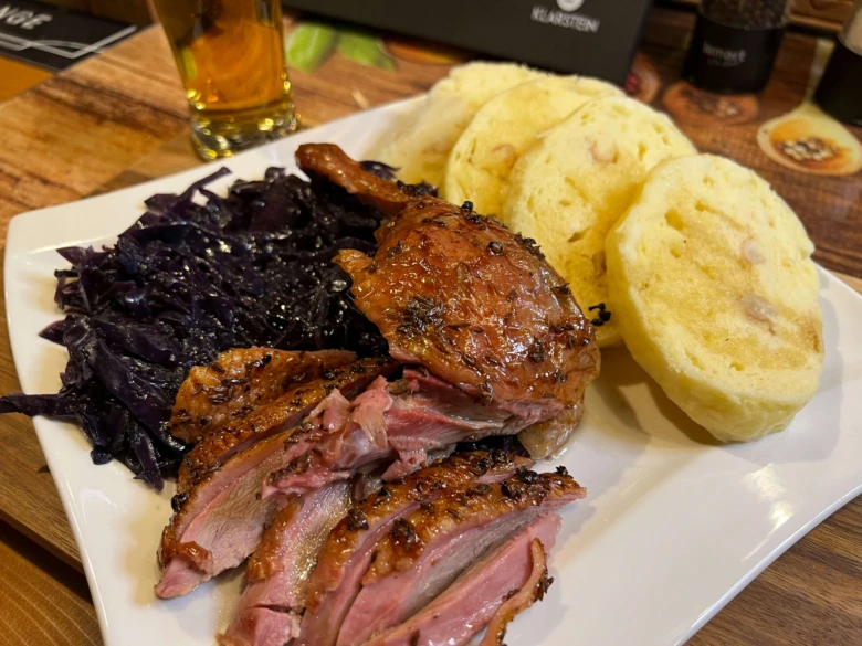 Grilovaná kachna s červenou kapustou a chlebem na talíři.