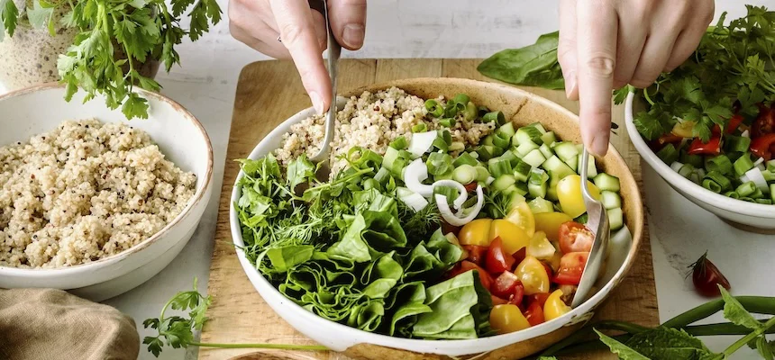 Veganský salát s kvinoou, zeleninou a rukama míchajícími v dřevěné mísce.