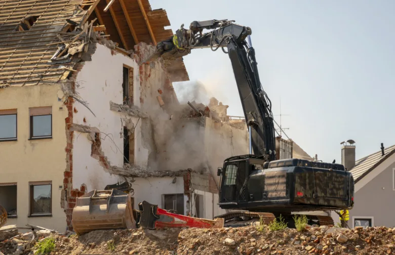 Buldozer rozebírá dům během bezpečné demolice.