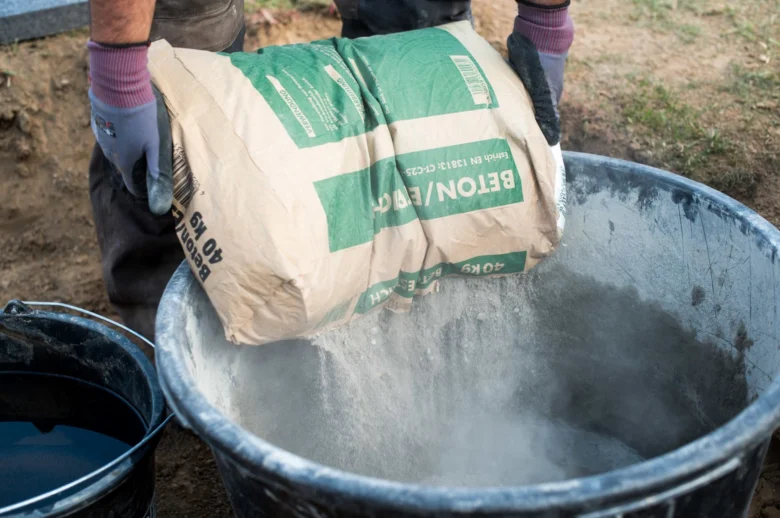 Muž nalévá cement z pytle do kbelíku pro stavební práce.