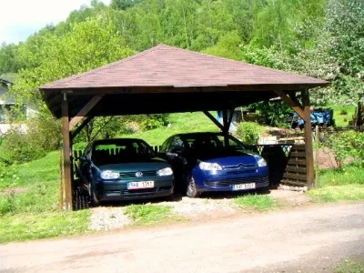Dřevěná pergola s dvěma auty pod ní na pozadí zelené přírody.