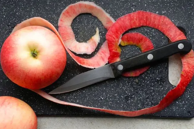 Červené jablko s kůrou a nožem na řezacím prkénku.