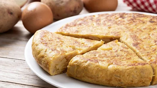Smaženka s bramborami a vejci na bílém talíři.