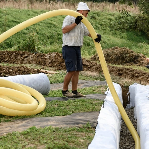 Muž odvádí dešťovou vodu žlutozelenými hadicemi.