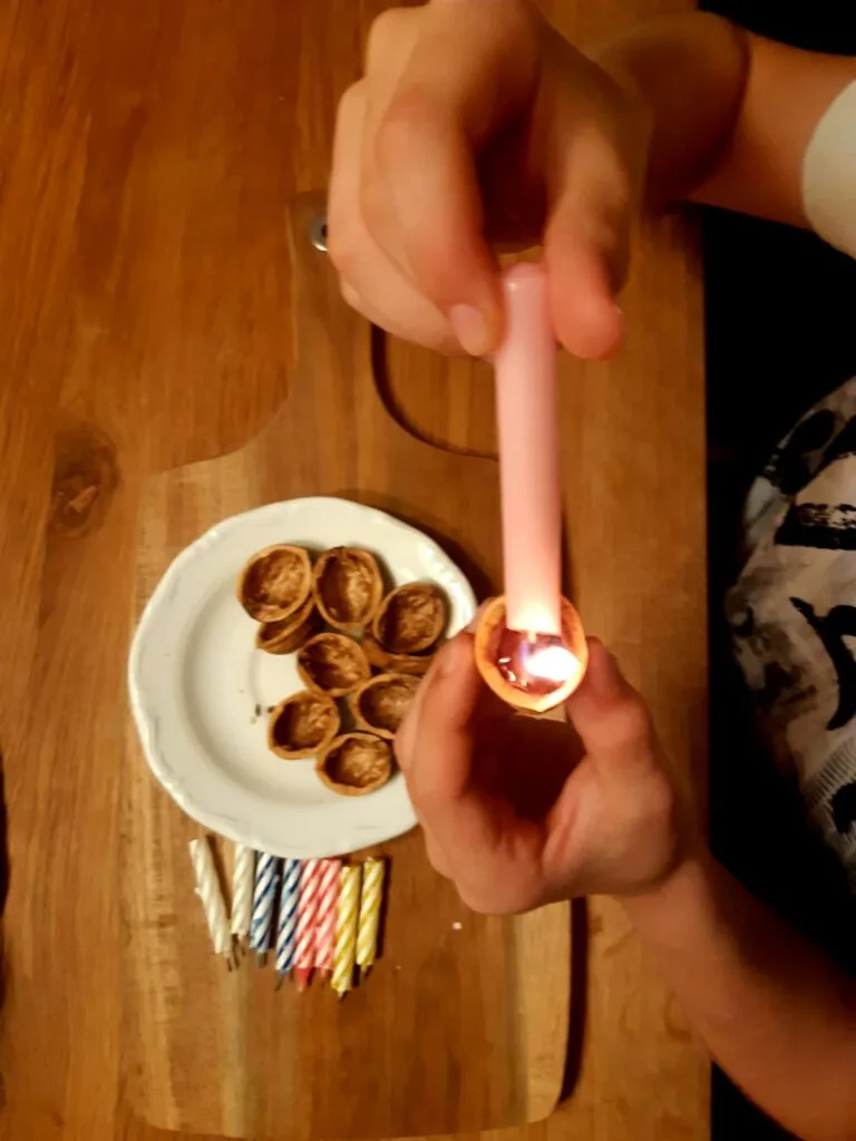 Ruce zapalují svíčku v skořápce oříšku na dřevěném stole.