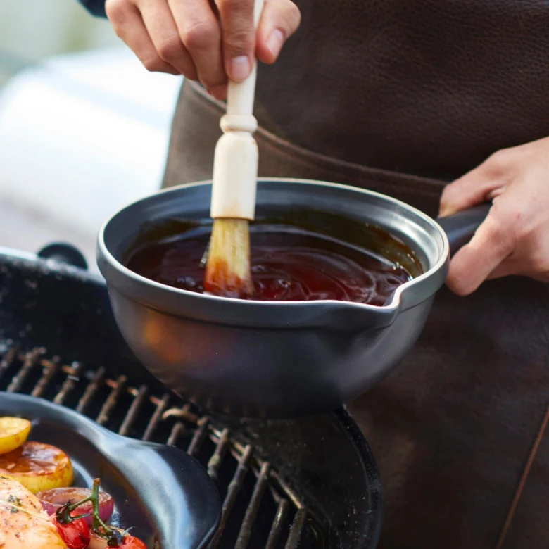 Osoba nanáší barbekýovou omáčku na grilované jídlo štětcem