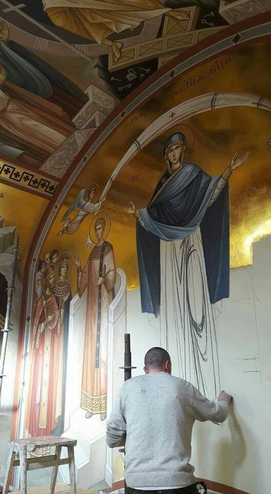 Umělec maluje fresku na zdi v kostele s dalšími postavami.