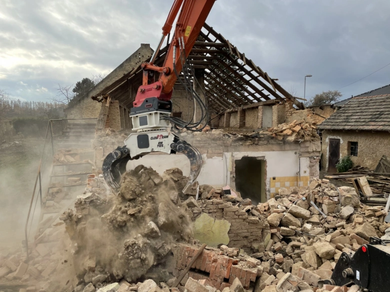 Brouk s hydraulickým úderákem rozebírá starý dům.