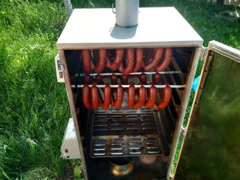 Klobásy se kouří v kovovém dýmovadle venku na trávníku.