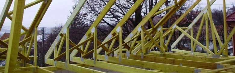 Žluté sbíjené vazníky na stavbě střechy.