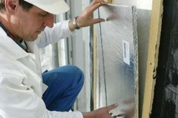 Montážní pracovník instaluje panel vakuové izolace do stěny.