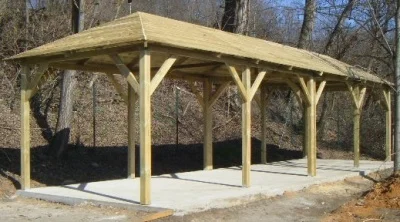Nová dřevěná pergola s plochou střechou na pozadí lesa.
