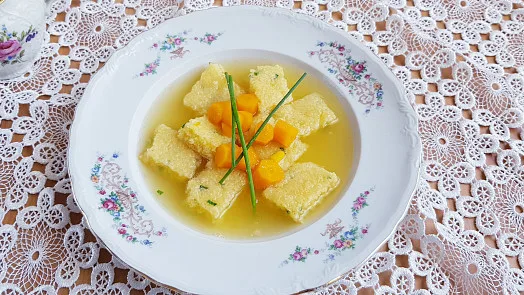 Polévka se svíčkovými knedlíky a mrkví na bílém talíři.