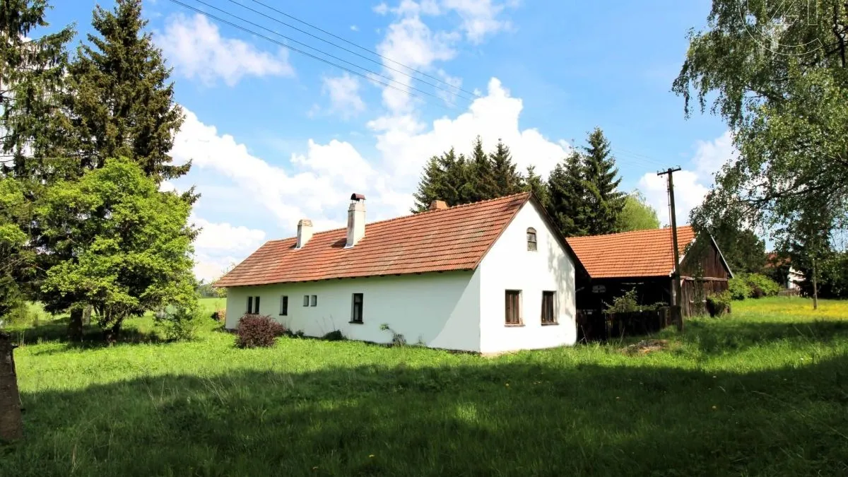 Bílá venkovská chalupa s červenou střechou na zelené louce.