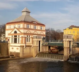 Malá vodní elektrárna na potoku s historickým domem.