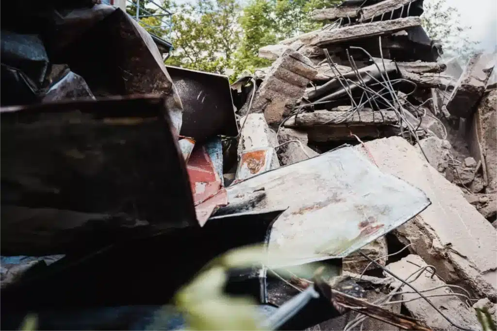 Zničený dům po demolici s betonovými bloky a ocelovým žebřím.