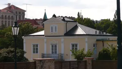 Žlutá historická vila Lumbeho s bílými okny a zeleným okolím.