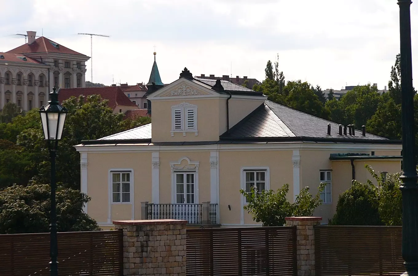 Žlutá historická vila Lumbeho s bílými okny a zeleným okolím.