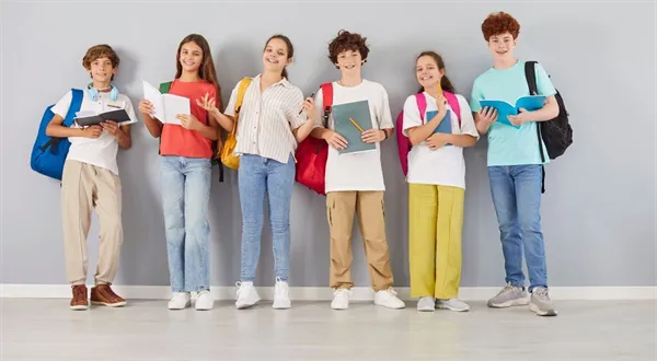 Šest šťastných studentů s batohy stojí v řadě u zdi.