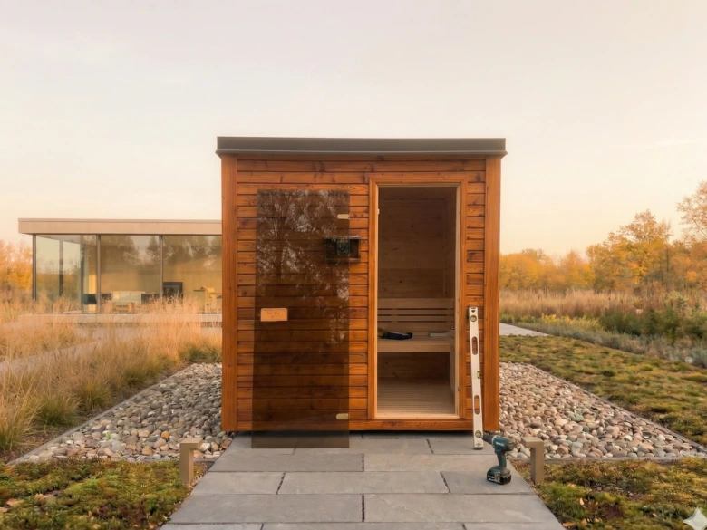 Dřevěná venkovní sauna s otevřenými dveřmi a nástroji uvnitř.