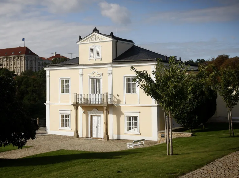 Žlutá Lumbeho vila s balkónem na zelené trávě.