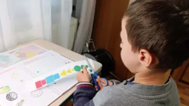 Chlapec řezá barevné tvary z papíru na stole.