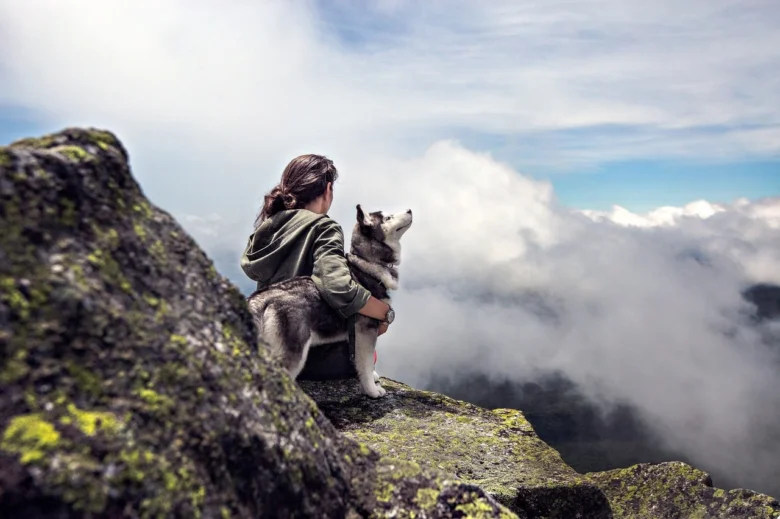 Žena sedí sibiřským huskym na skále nad mraky.