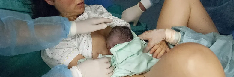 Matka drží novorozence po porodu s pomocí lékařů.