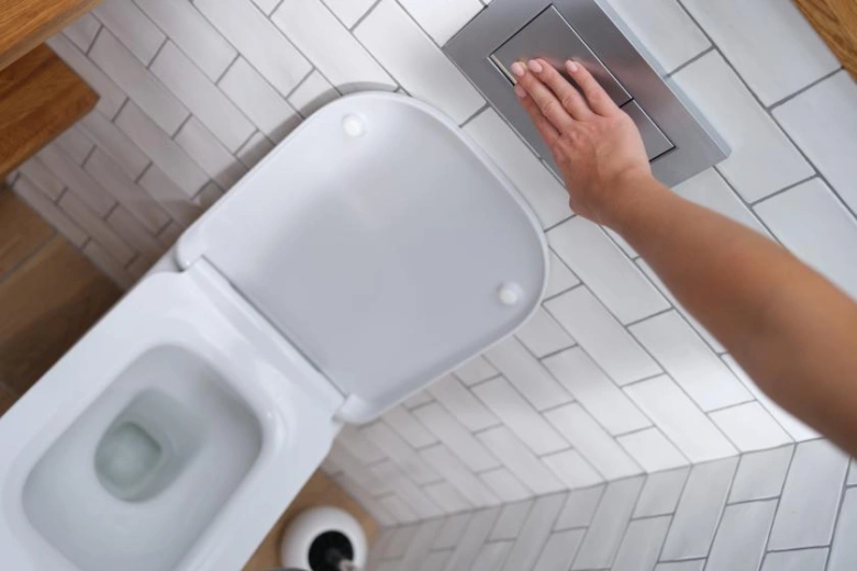 Ruka tlačí na spoušť WC s otevřeným poklopem.