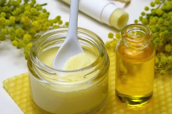 Propolis v nádobě s lžící, olejová láhev a propolové květy na žlutém podkladu