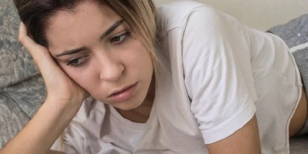 Žena leží na gauči s výrazem bolesti nebo úzkosti.