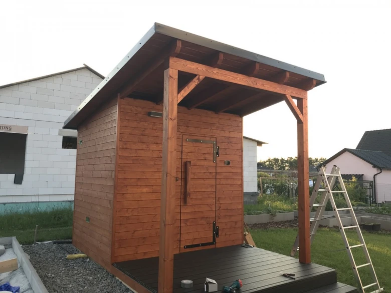 Dřevěná sauna v stavbě s otevřenou terasou na zahradě.