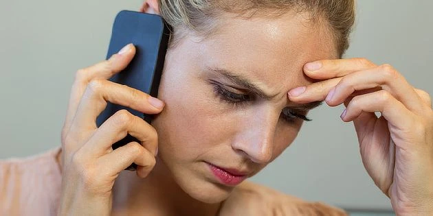 Stresovaná žena na telefonu s rukou v čele.